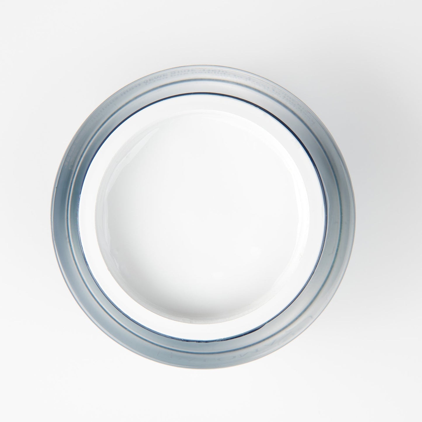 Top view of an open, transparent, circular jar filled with white builder gel, revealing a dense and creamy texture. The jar is placed against a pristine white backdrop, suggestive of a professional studio setting.