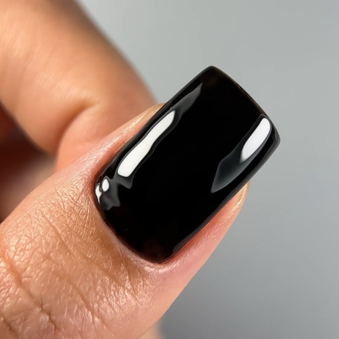Close-up of a fingernail painted with Paloma's long-lasting, highly-pigmented gel nail polish in shade C002, a deep, intense black color. Finished with Paloma Shine Top Coat for a glossy, durable look, perfect for a sophisticated and bold gel manicure.