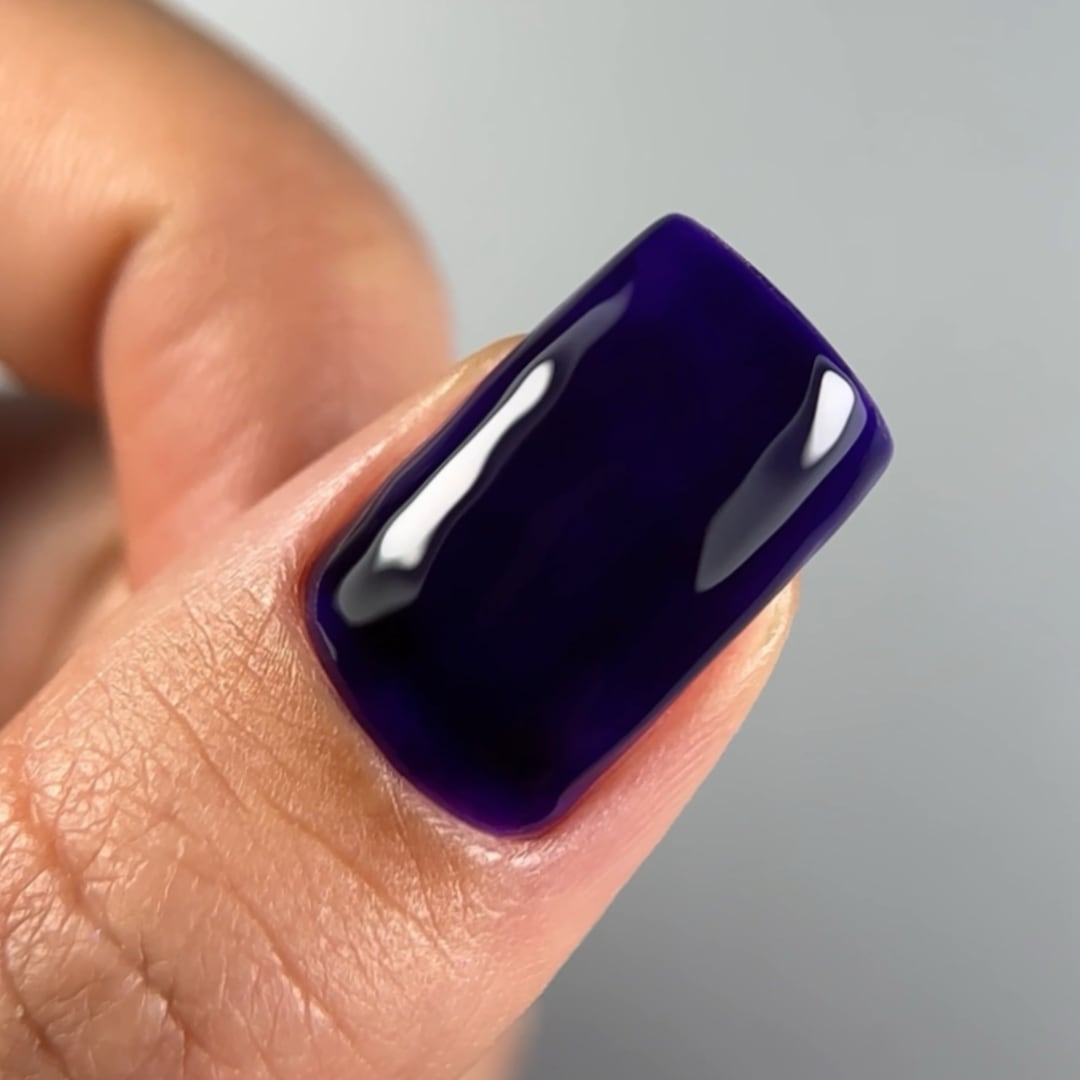 Close-up of a fingernail painted with Paloma's long-lasting, highly-pigmented gel nail polish in shade C051, a deep purple color. Finished with Paloma Shine Top Coat for a glossy, durable look, perfect for a sophisticated and bold gel manicure