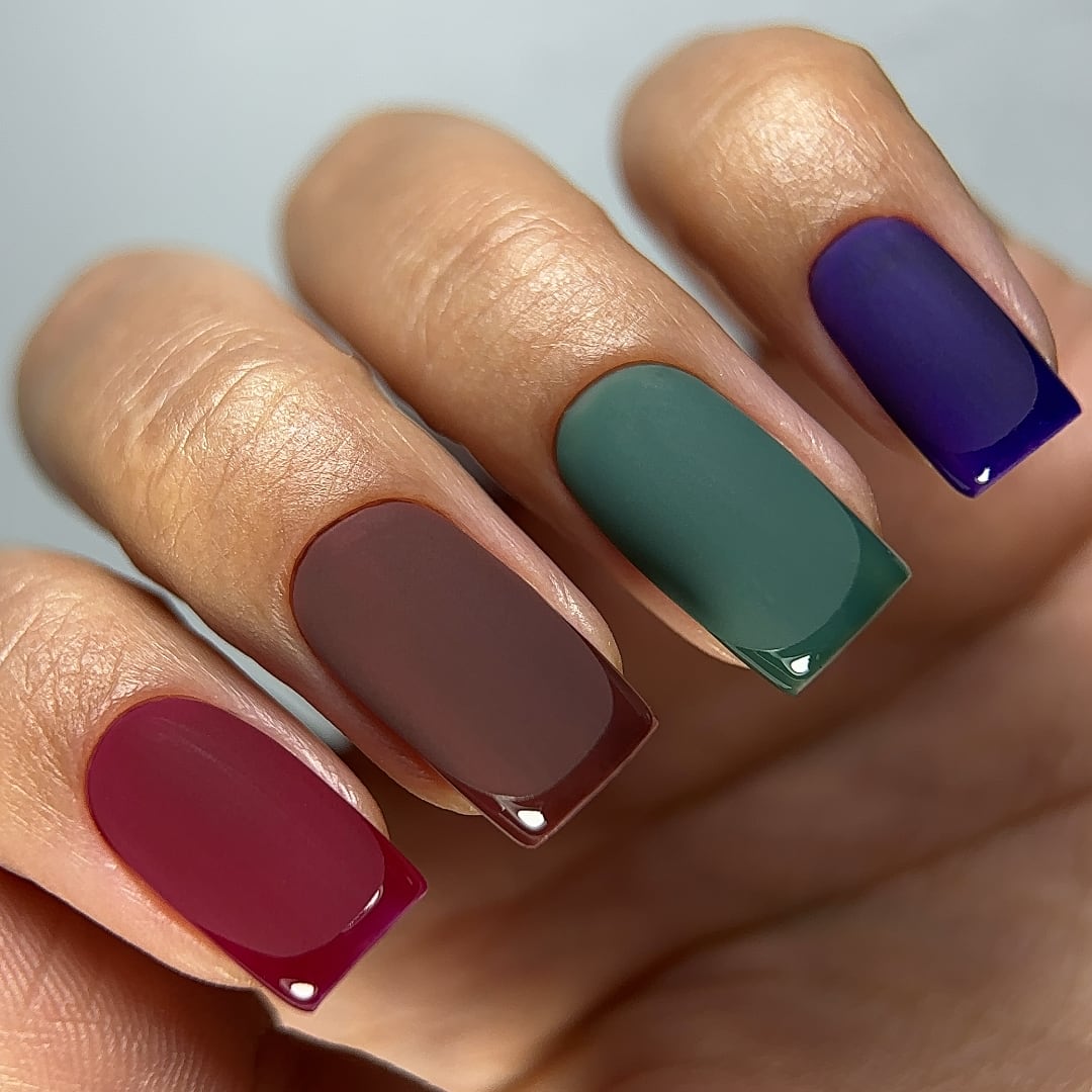 Close-up of a French manicure featuring colors from Paloma's Mystery Forest gel polish collection, including burgundy, chocolate brown, green, and deep purple. Each nail has a matte finish with glossy tips, showcasing the rich, highly-pigmented shades. This collection offers five long-lasting gel polishes for the price of four, perfect for creating bold and sophisticated nail art.